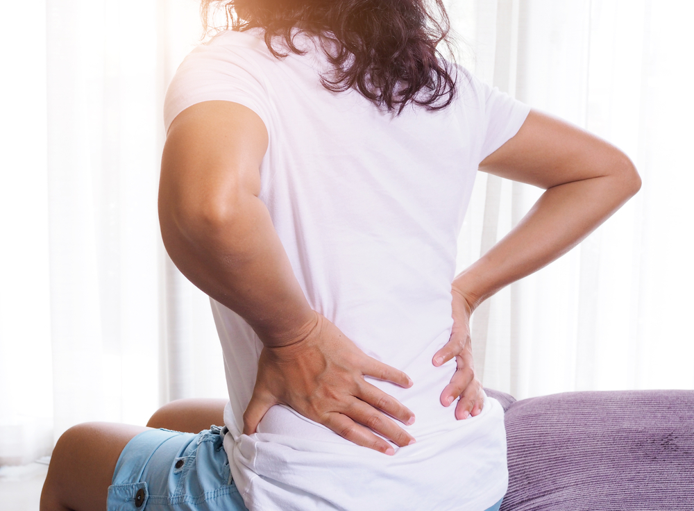 A woman is sitting with her hands on her back as if in pain.