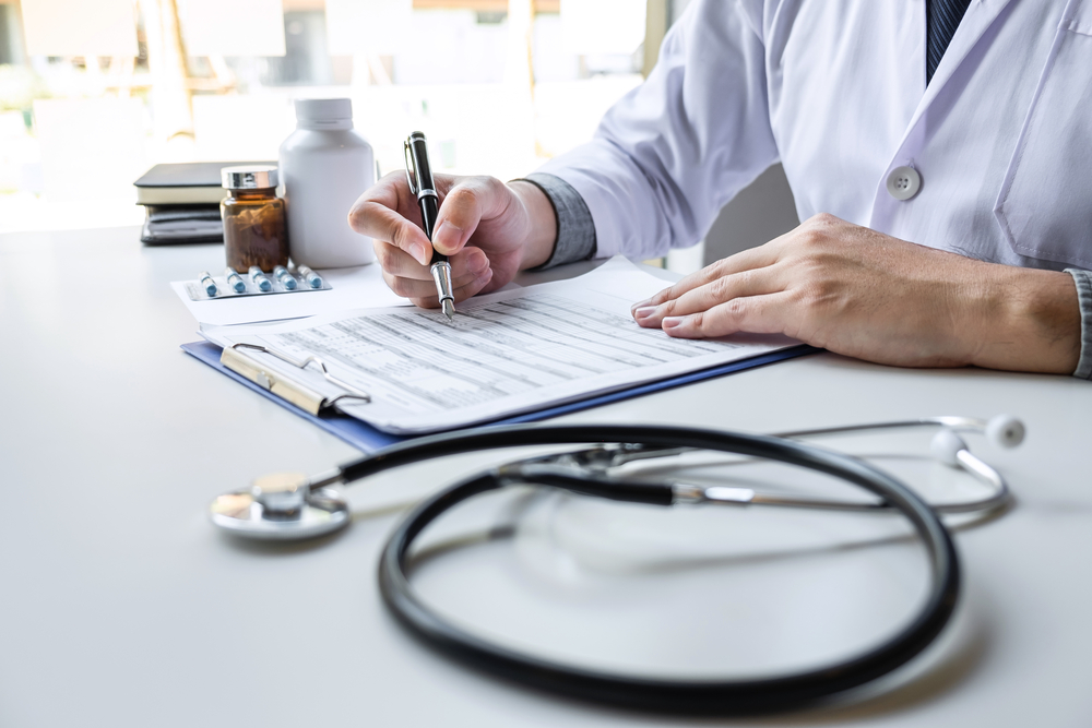 A physician looking over a form at his desk with medical items around it.